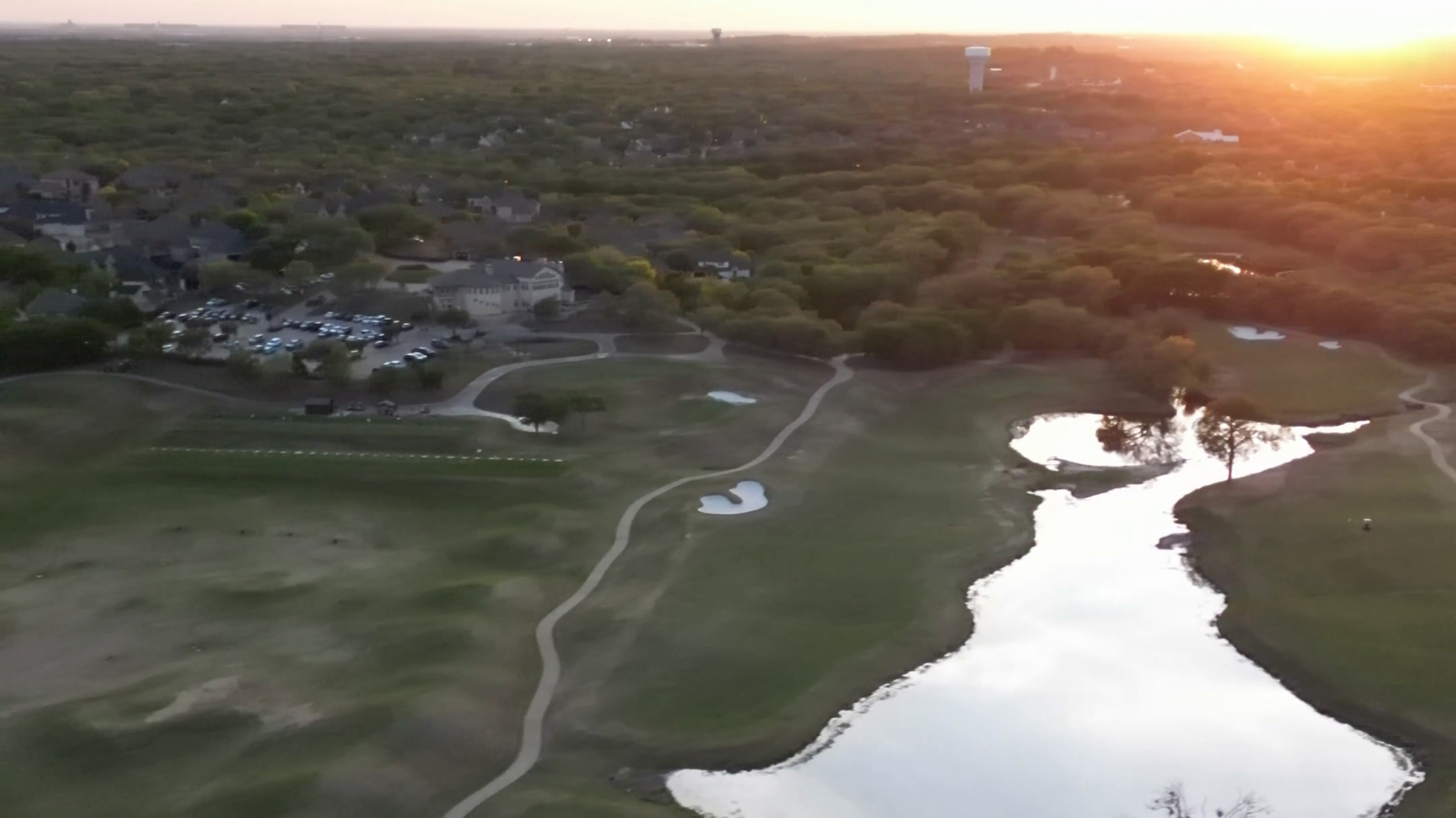 A golf course at sunset: fairways, water and the clubhouse under a low sun.